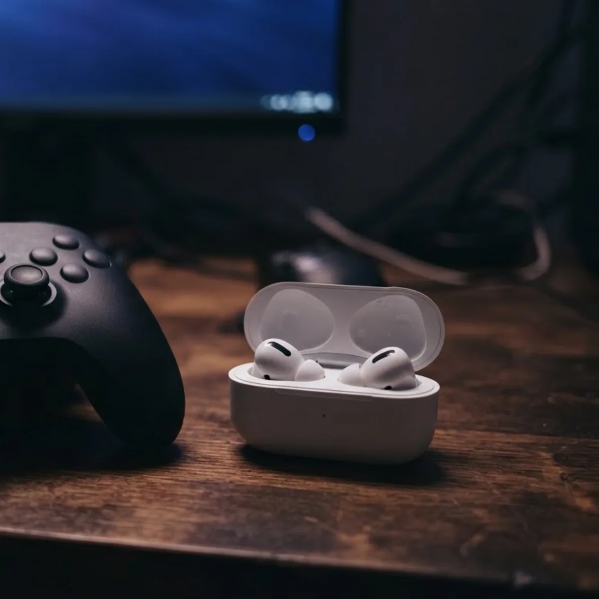 Game controller next to an open white earbuds case on a dark gaming desk