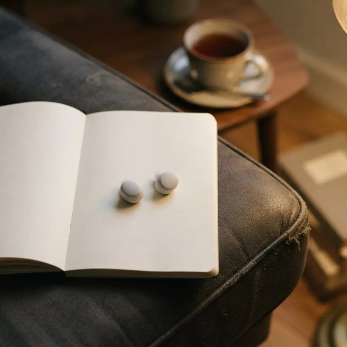 Two white earbuds lying on an open notebook by a reading lamp