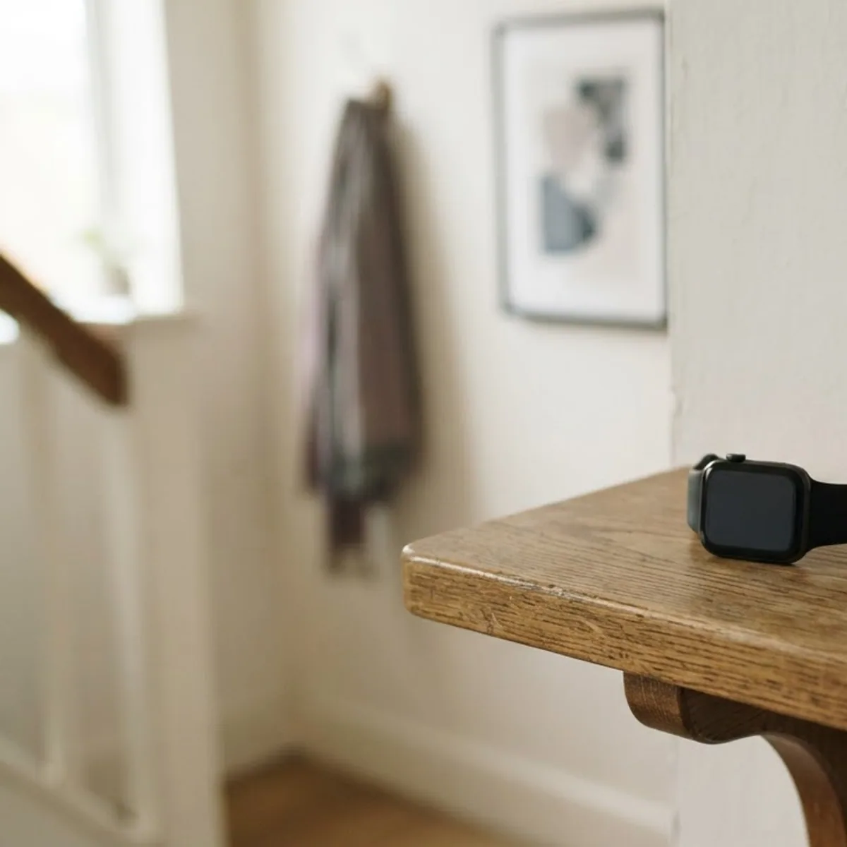 A smartwatch lying on a wooden entryway shelf next to a set of keys and a potted succulent