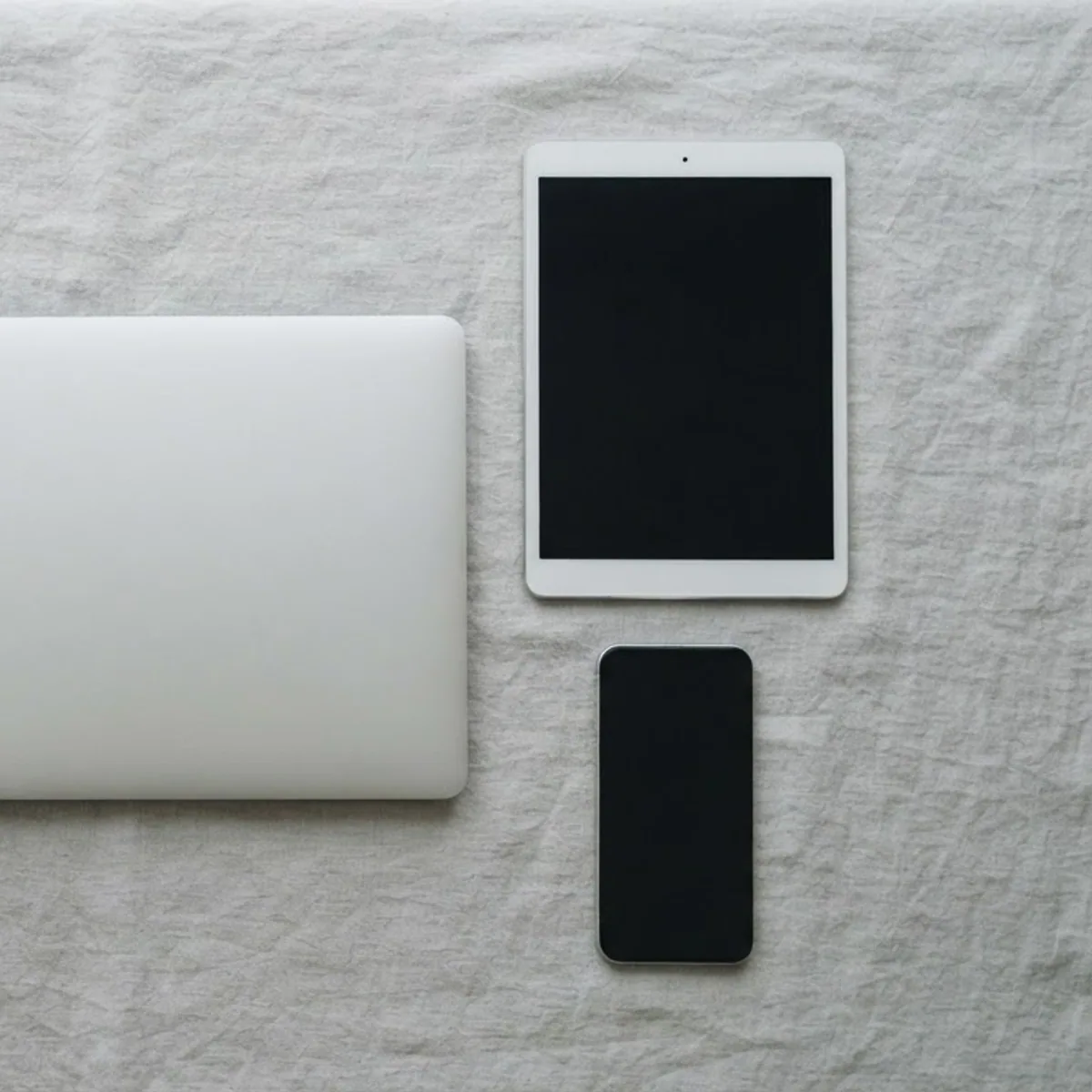 White over-ear headphones laid out next to a closed laptop, a tablet and a phone