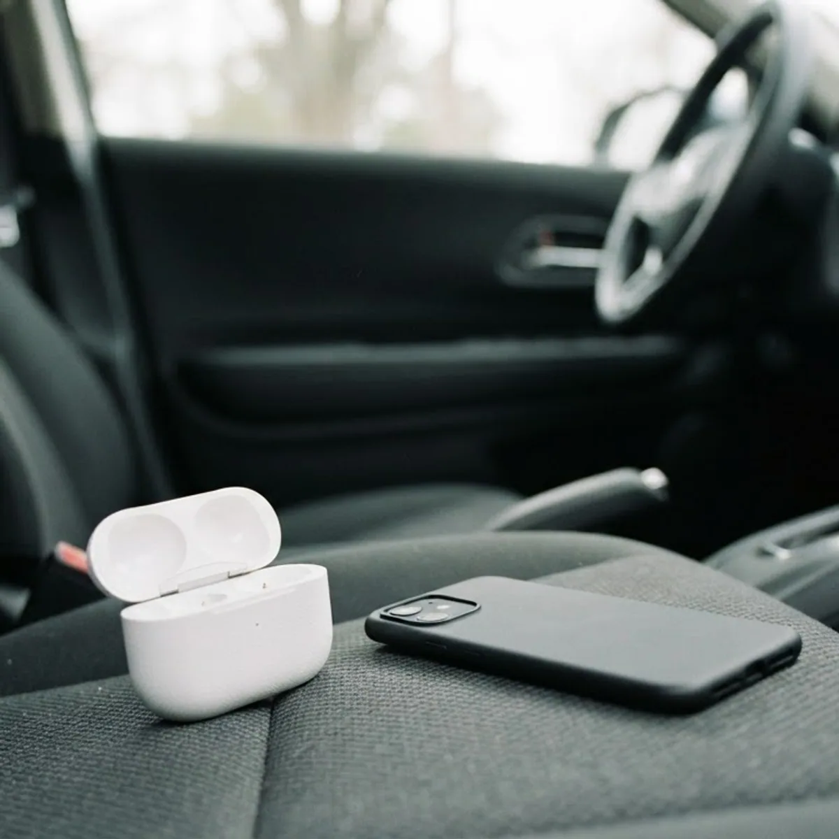 Open white earbuds case and a face-down phone on the passenger seat of a parked car