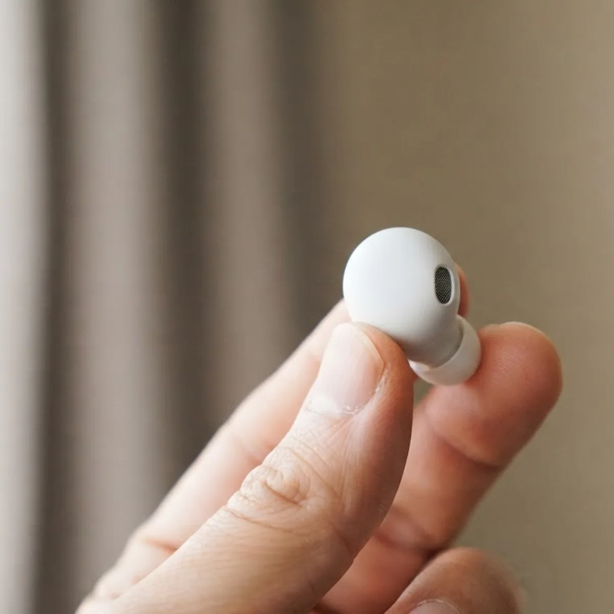 Hand holding a single white earbud between thumb and finger in soft window light