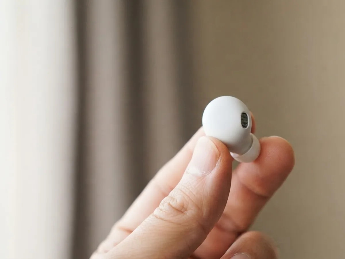 Hand holding a single white earbud between thumb and finger in soft window light