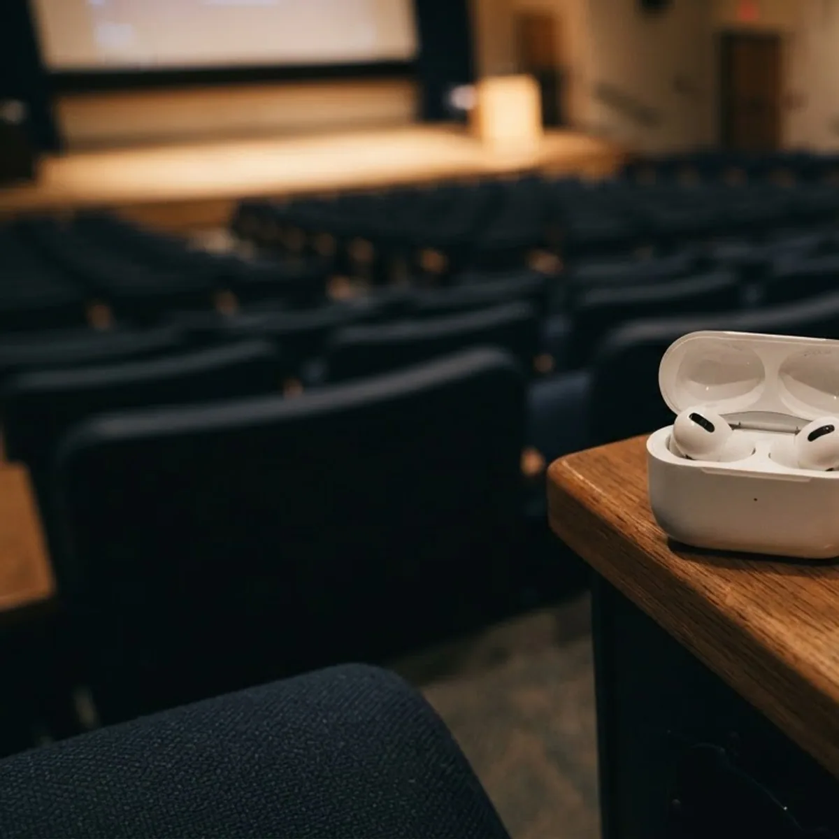 Open white earbuds case on the wooden armrest of a seat in an empty lecture hall
