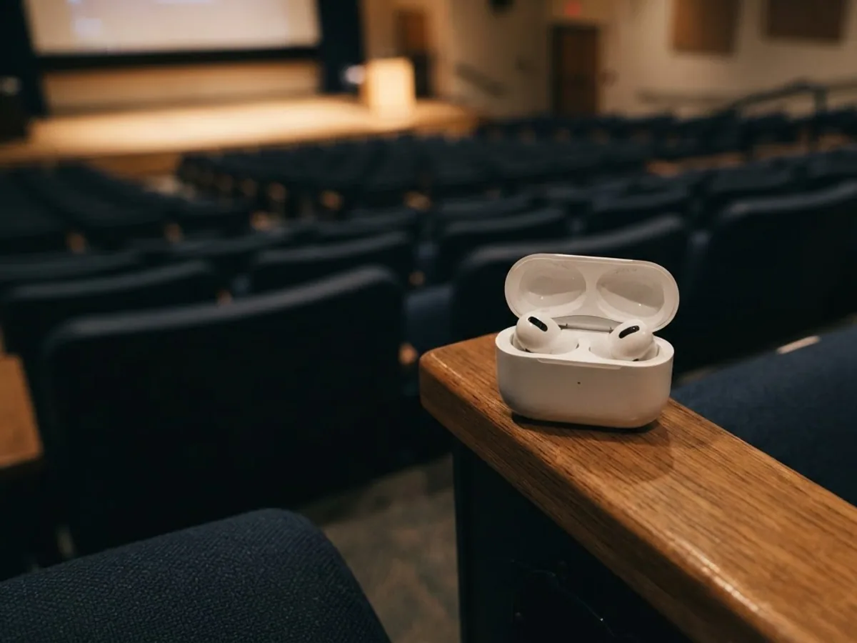Open white earbuds case on the wooden armrest of a seat in an empty lecture hall