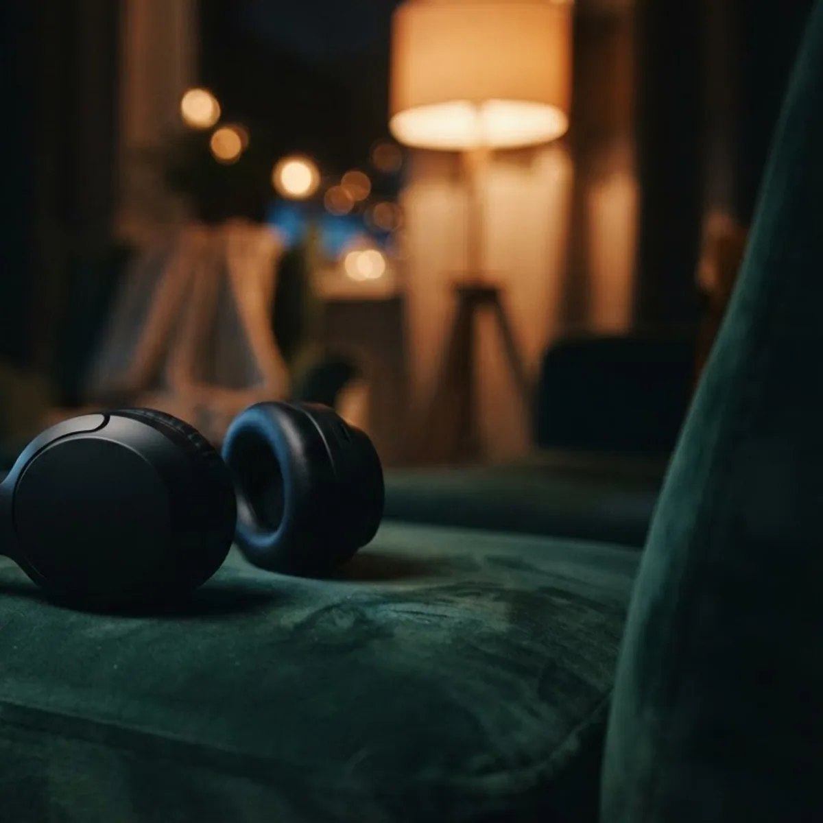 Black over-ear headphones resting on a green velvet armchair in a dim living room
