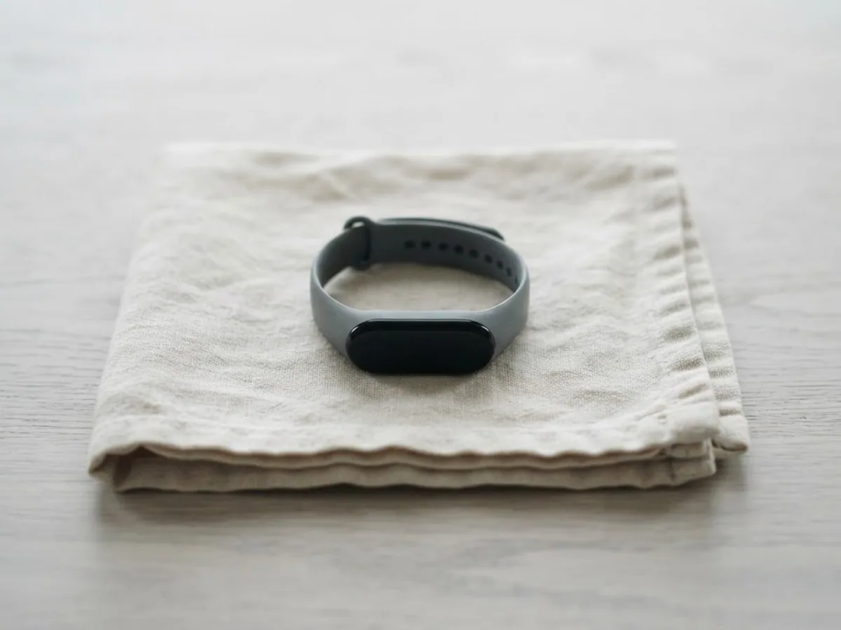 A slim fitness tracker with a grey band resting on a folded linen cloth on a pale wooden table