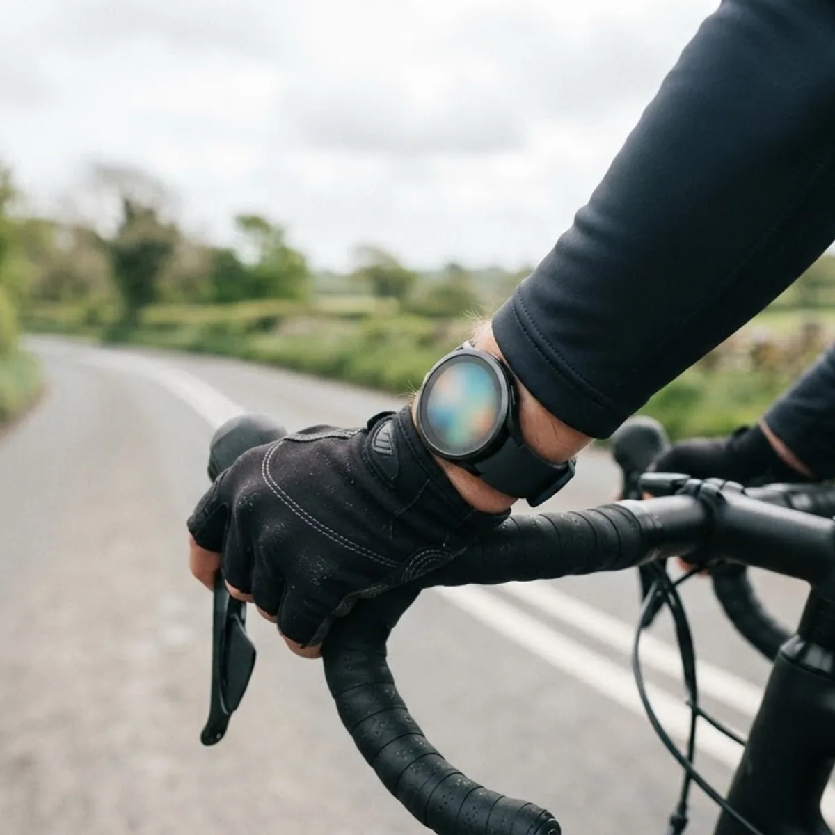 A cyclist's gloved hand on a road bike handlebar with a round sports watch lit up on the wrist