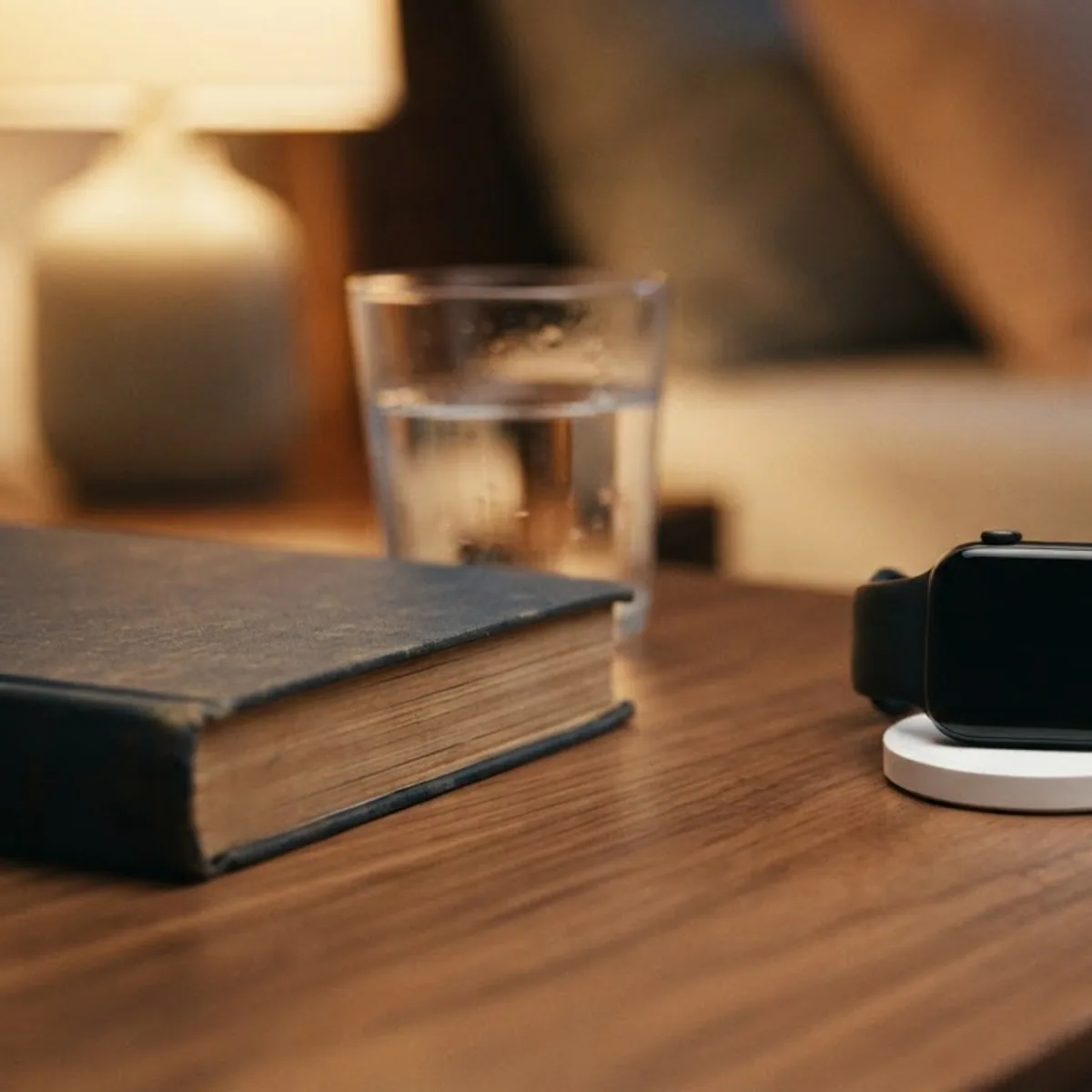 Smartwatch sitting on a round charging pad on a bedside table at night